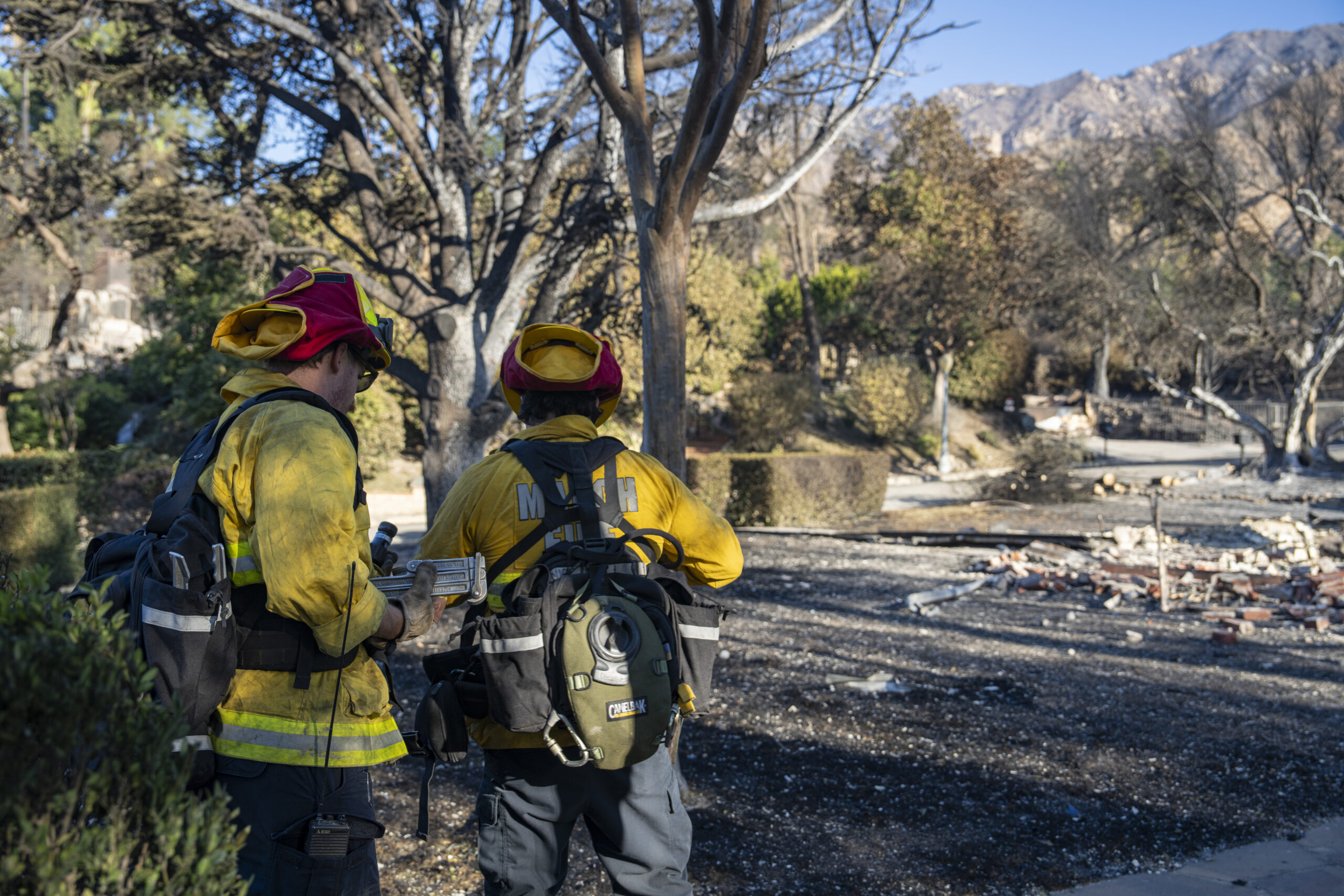 Firefighting and emergency personnel assess the damage among the ashes